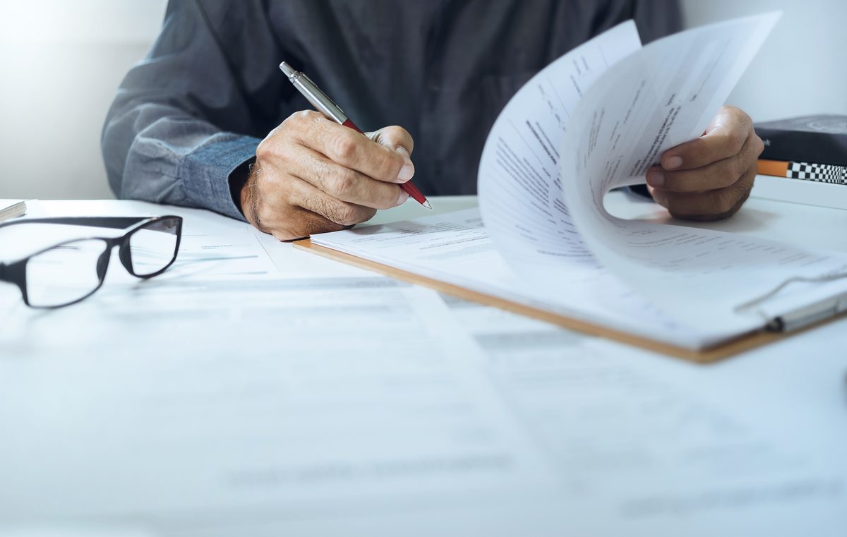 صورة توضيحية لشخص يراجع أوراقاً بقلم على مكتب، دون ظهور الوجه